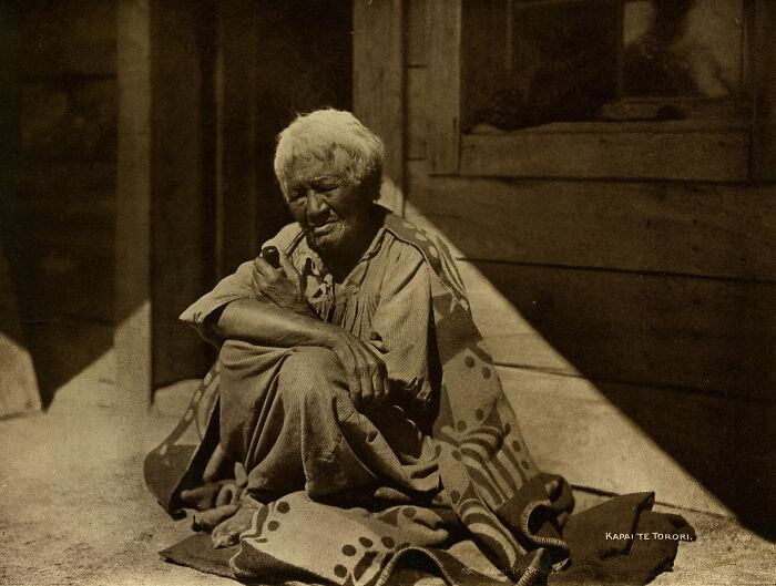 Portrait Of Maori Woman With Facial Moko (Tattoo); Seated In Front Of House, Holding Pipe